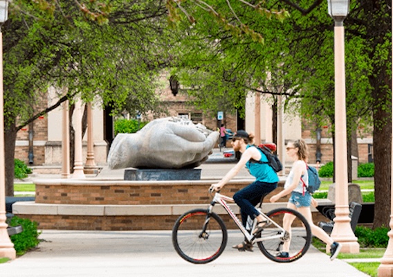 person on bike and person walking past the hands fountain on campus