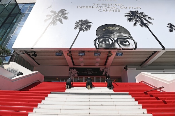 workers laying a red carpet on the steps of the Cannes building