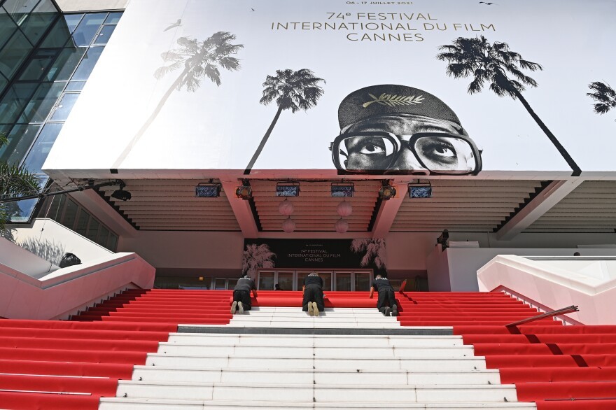 workers rolling red carpet down the Cannes building's stairs