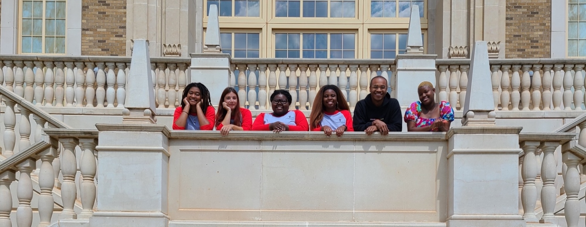 Six students looking at the camera while standing on a stonework balcony