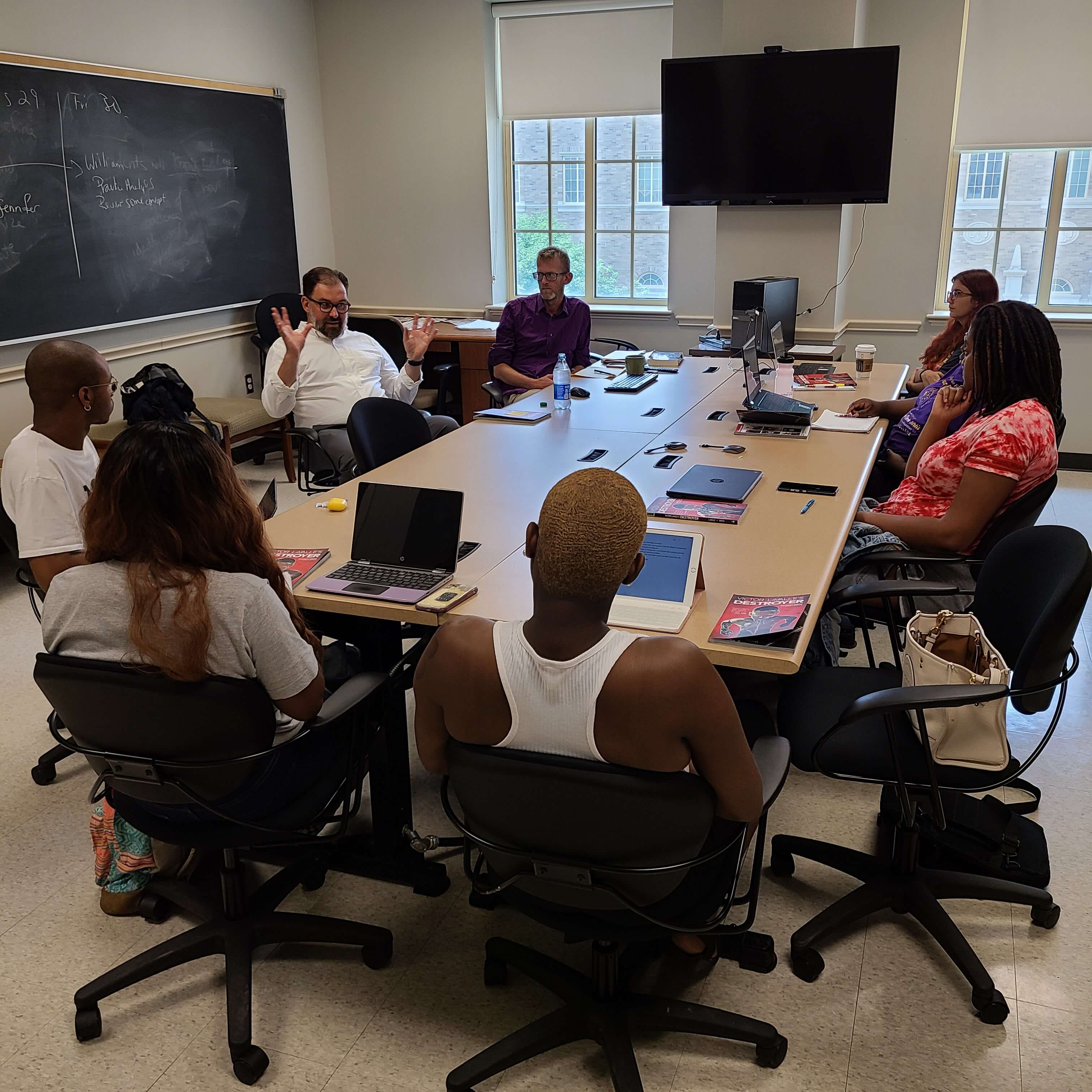 students and teachers sitting around a table discussing a text