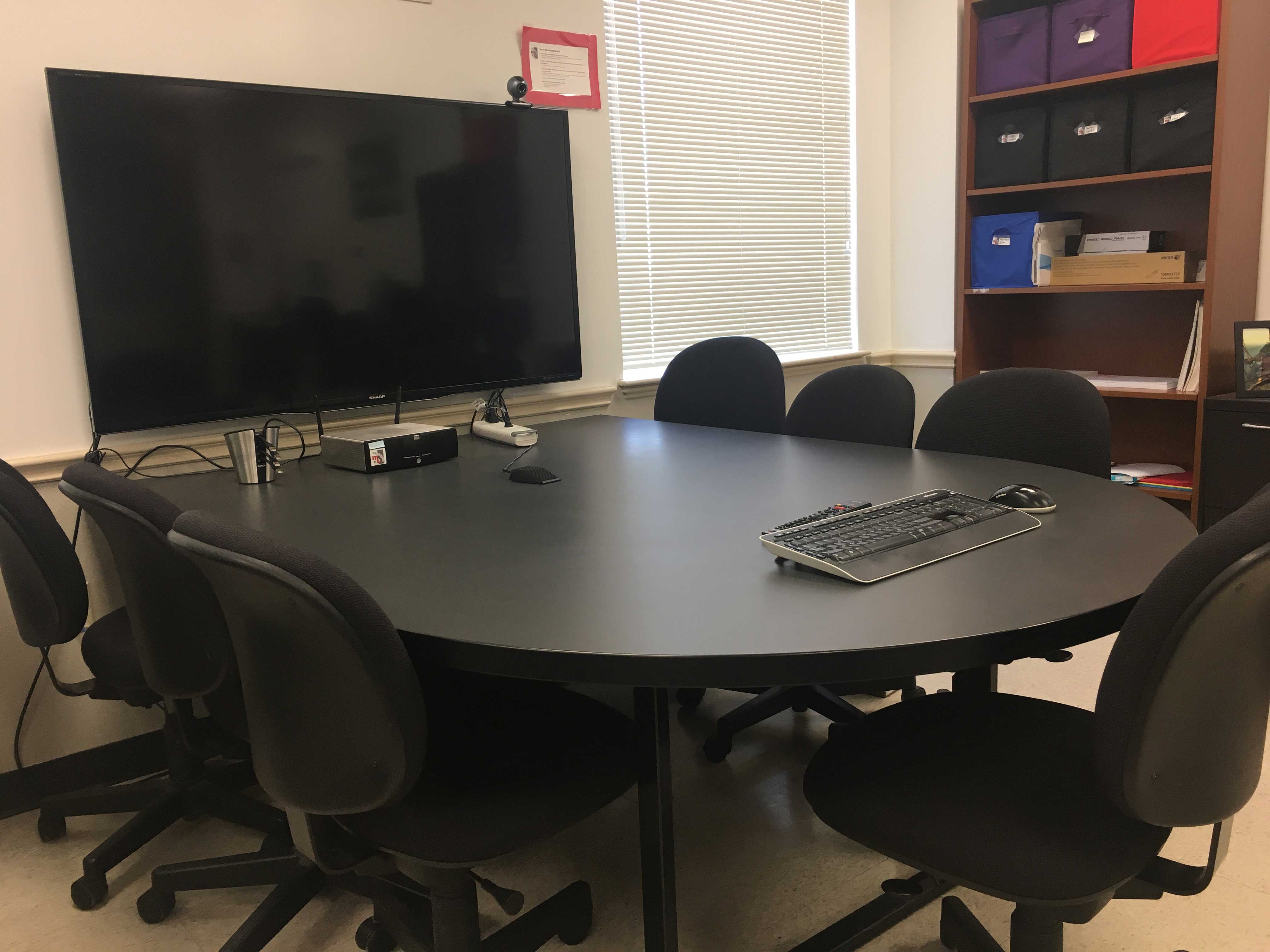 Conferene Area table surrounded by chairs with large TV mounted on wall