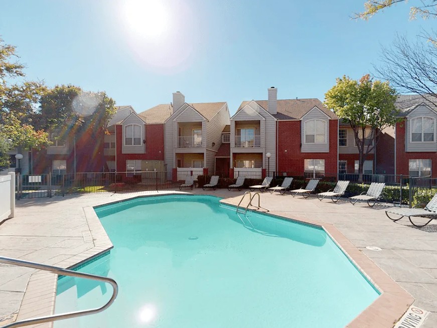 Outdoor swimming pool at Ashton Pointe with lounge chairs and apartment buildings in the background.