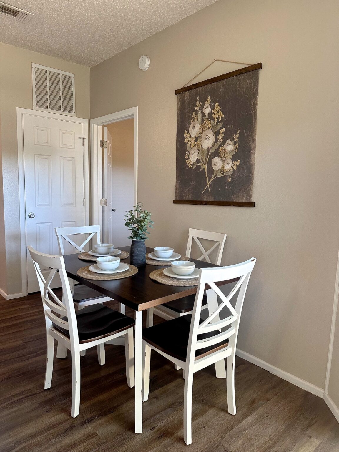 Dining area with table set for four and floral wall decor.