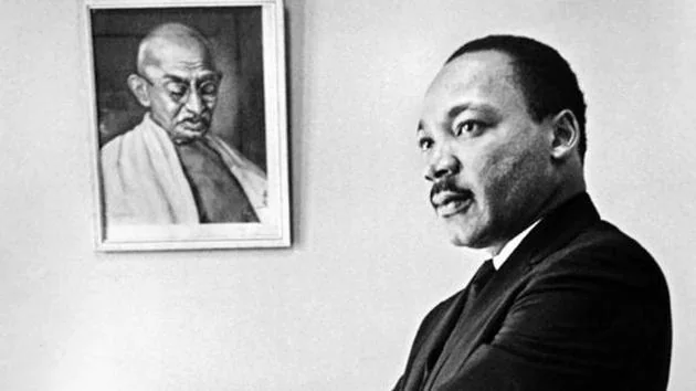 Martin Luther King Jr. standing in front of framed picture of Mahatma Gandhi