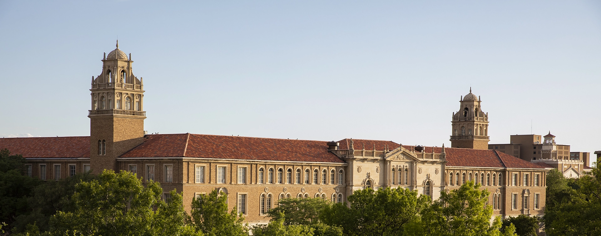 The Texas Tech Admin Building framed by green trees along the bottom edge of the image.