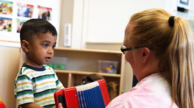 Center for Early Head Start student and teacher playing with toy accordion