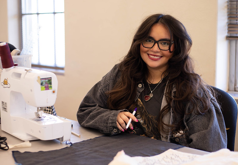Alizandra Castillo smiling at the camera and sitting at a table with a sewing machine