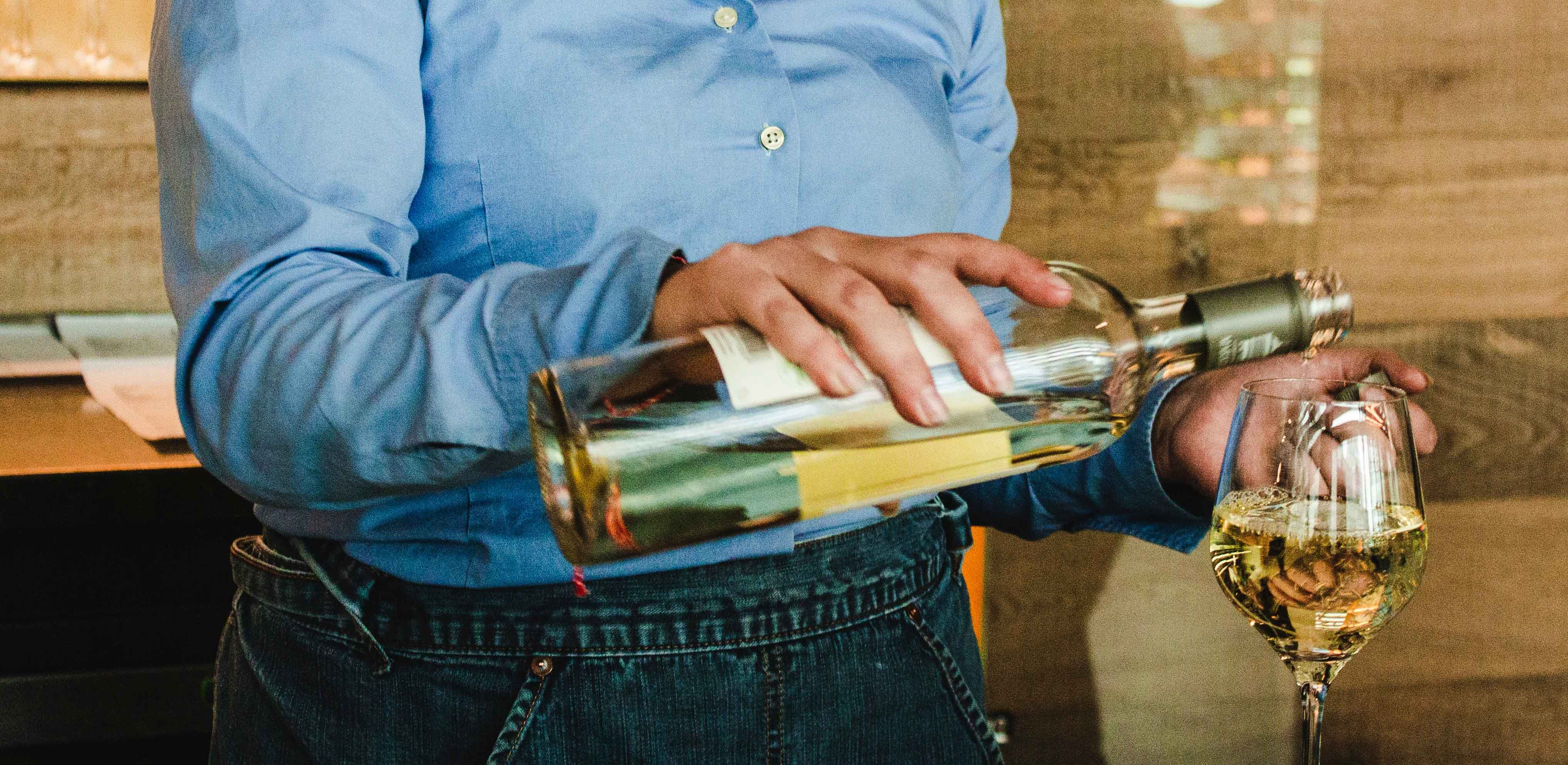 server pouring white wine into glass server pouring white wine into glass
