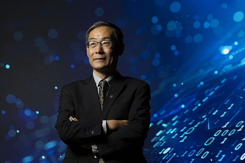 CIO Dr. Lin Zhou posing with a blue digital looking background with 0's and 1's in the background.