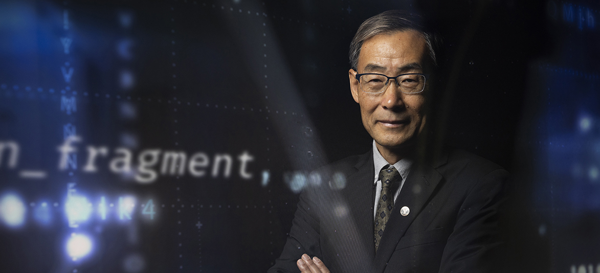CIO Dr. Lin Zhou posing in front of a dark background with technology elements subtly in view around him.