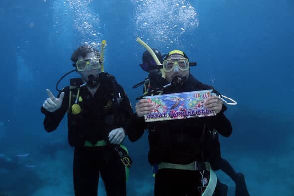 Two students underwater in scuba gear making a guns up symbol