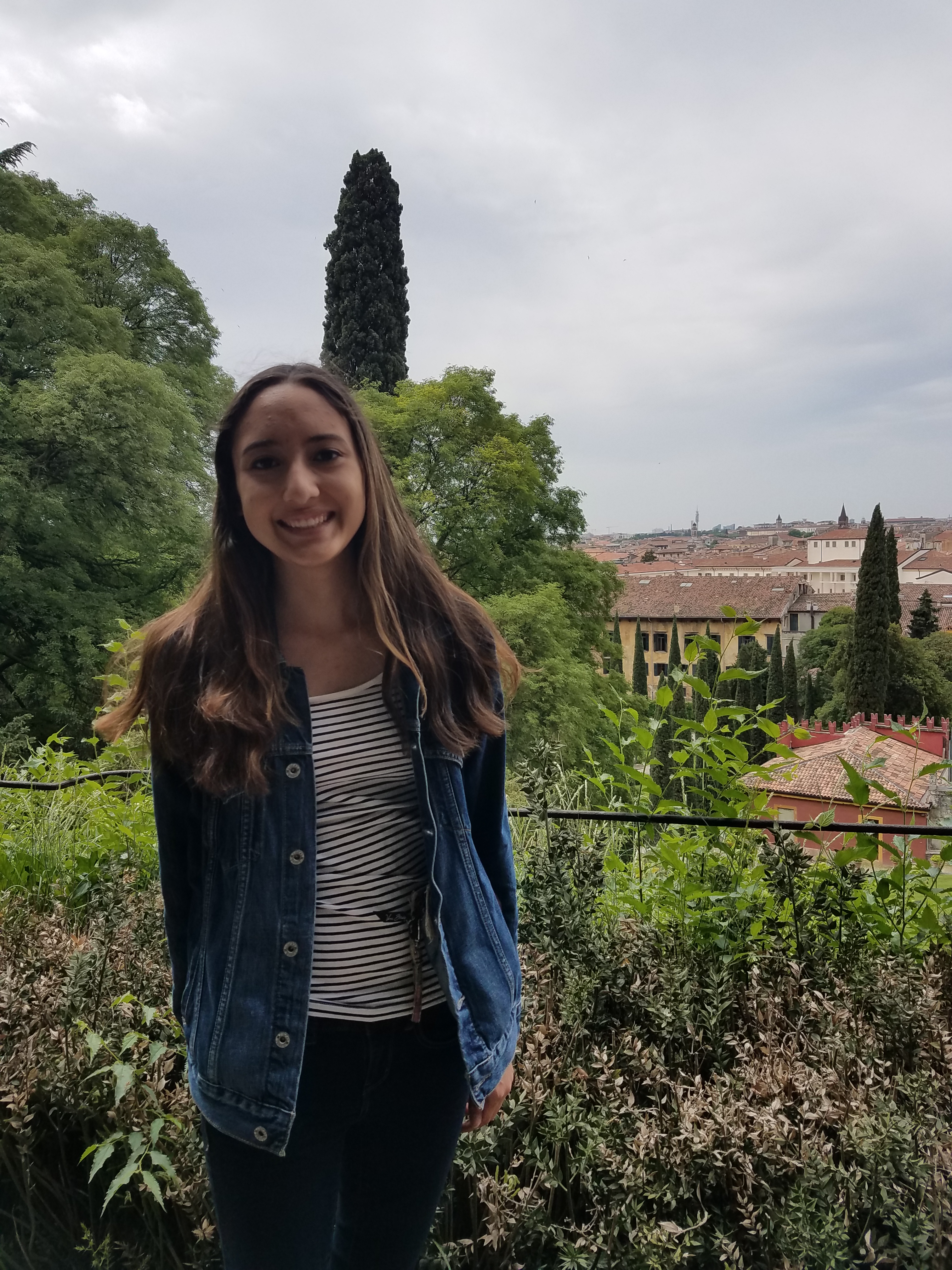 Woman standing in front of green trees and bushes.