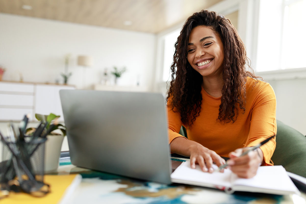 Online student. Smiling woman sitting at desk, using a laptop.