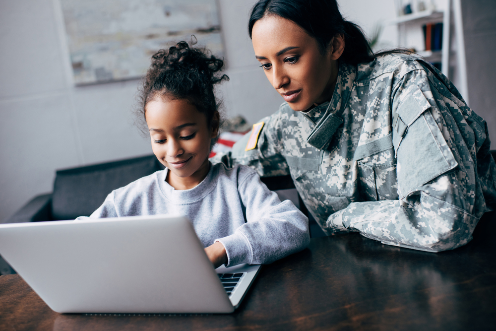 Photo of mother in military uniform with daughter in front of a laptop.