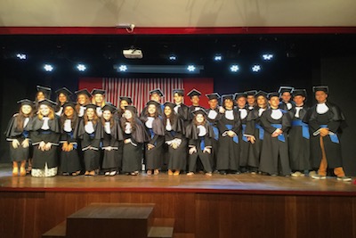 TTU K-12 graduates pose in black caps and gowns on stage.