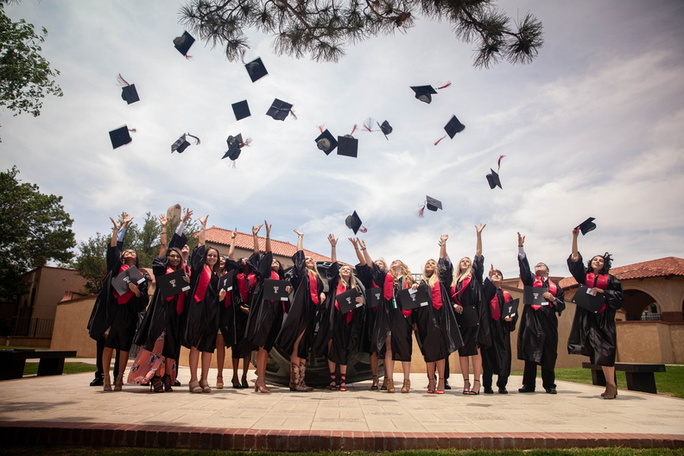 Representatives of the 2018 TTU K-12 graduates toss their graduation caps into the air with outstretched arms as they stand on a concrete slab outside