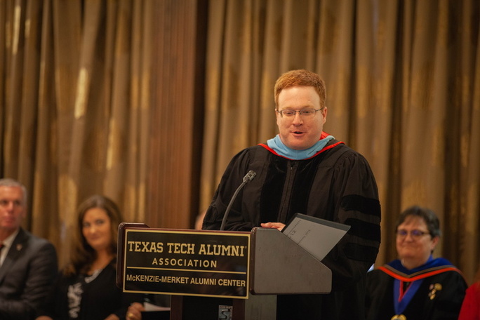 Dr. Justin Louder addresses the commencement participants Justin Louder stands behind a podium while addressing his audience
