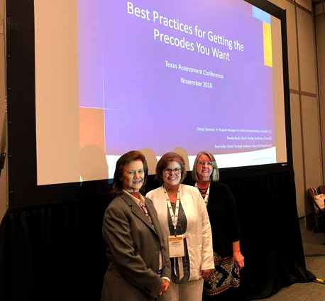 Pam Butler stand alongside Christy Sassman and Brenda booth in front of a projector screen smiling and looking at the camera