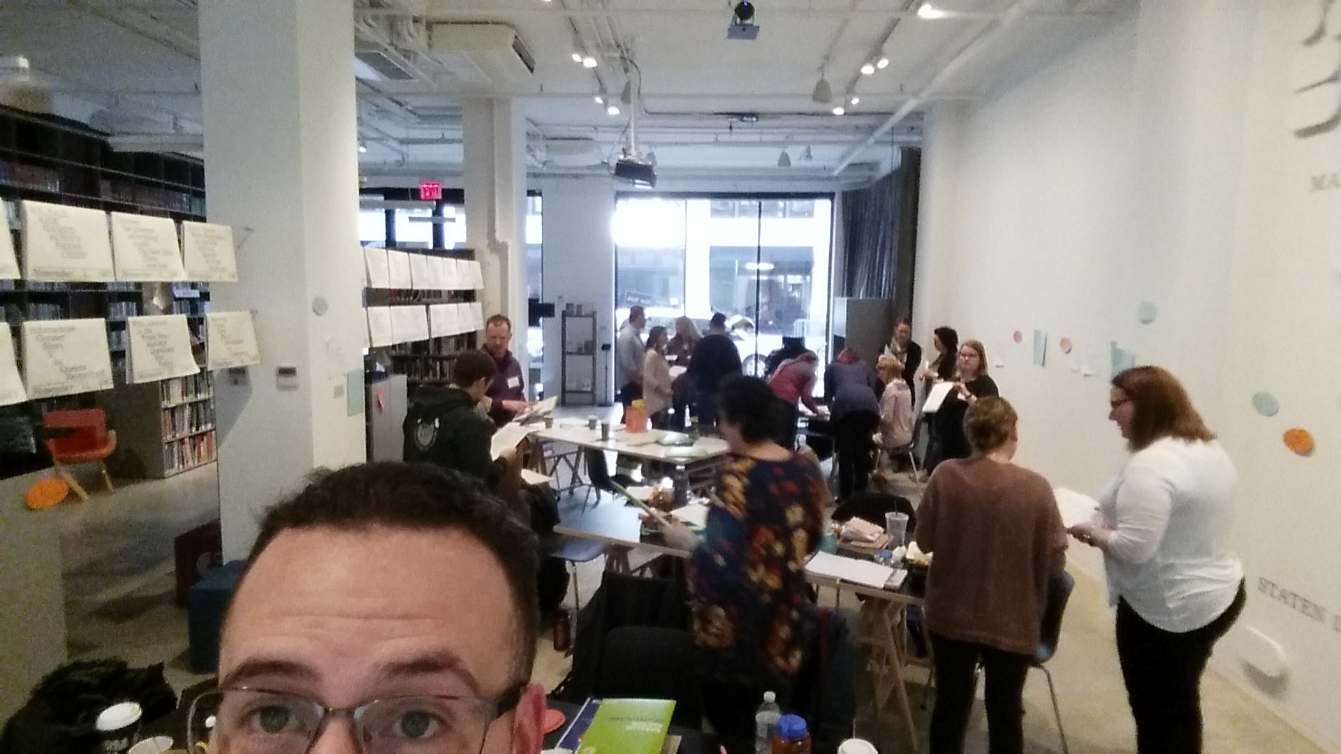 The cohort of teachers work together at the Goethe Institute in New York City. Jeremy Hogan stands in the foreground facing the camera while numerous teachers in the background work around several rectangular table