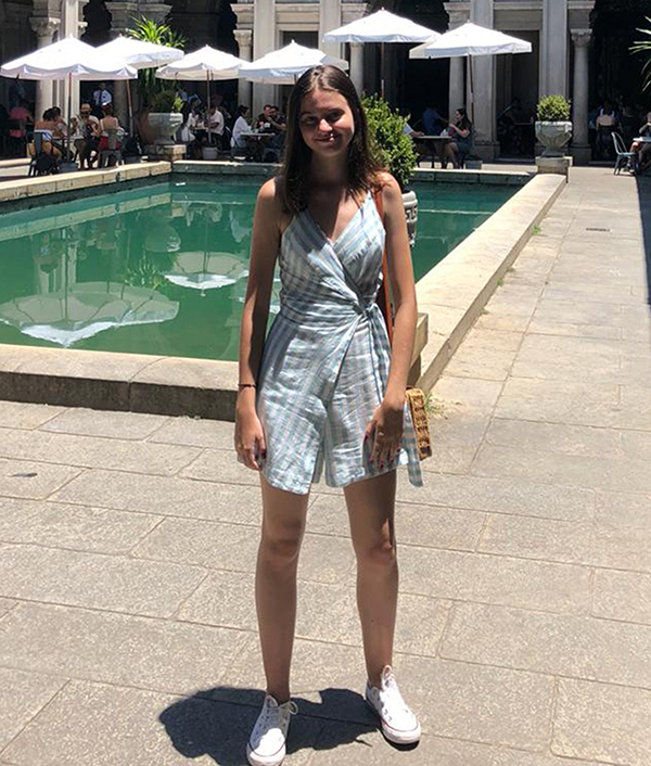 Gabrielle Dytz stands near a pool wearing a blue-stripped dress with people sitting at tables in the background.