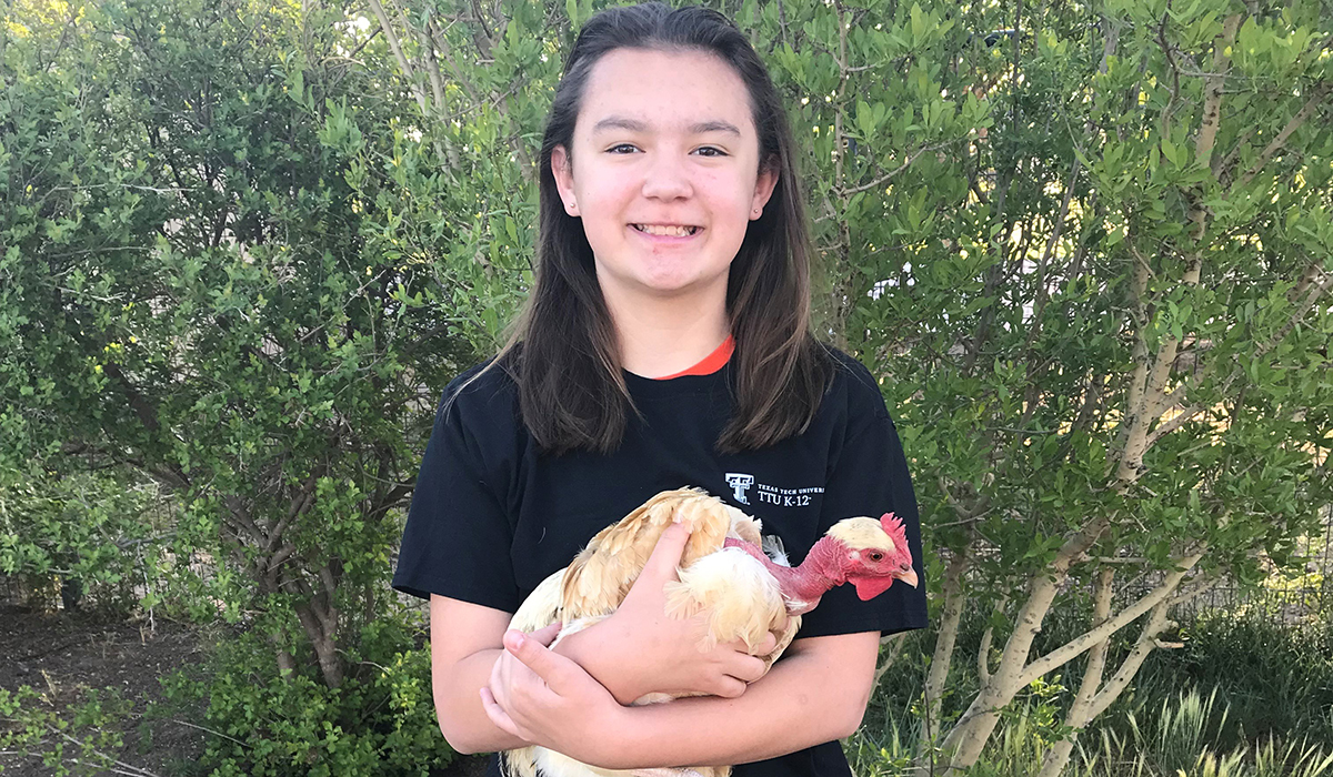 Logen poses with one of her 11 chickens. Logen Lee stands in front of greenery while holding a chicken in her arms and smiling.