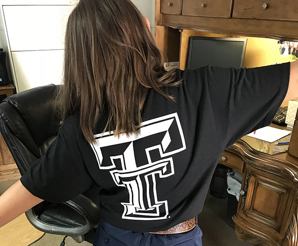 Logen sports her TTU K-12 shirt. Logen Lee poses in an office with her back facing the camera and wearing a Texas Tech shirt with the logo visible.