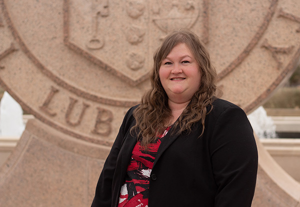 Crystal stands in front of the Texas Tech seal on campus wearing a black blazer with a black and red shirt.