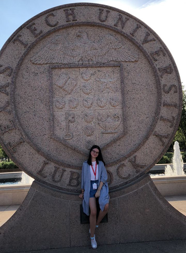 Crystal stands in front of the Texas Tech seal on campus wearing a black blazer with a black and red shirt.
