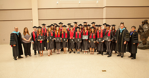 TTU K-12 students stand beside one another wearing their graduation caps and gowns 