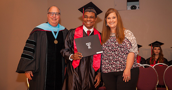 A TTU K-12 graduate student smiling and standing between Jim Taliaferro and Cari Moye