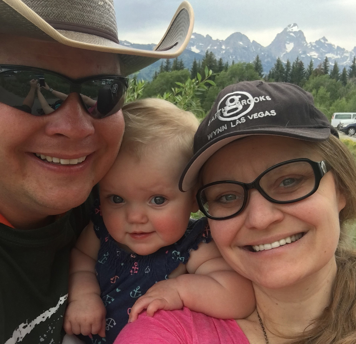 Laina scrunches next to her baby daughter in between her and her husband as they all face the camera while standing outside