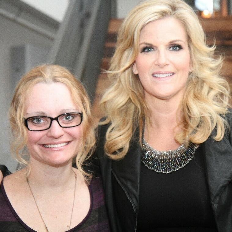 Laina and Trisha stand side by side inside a building while facing the camera and smiling