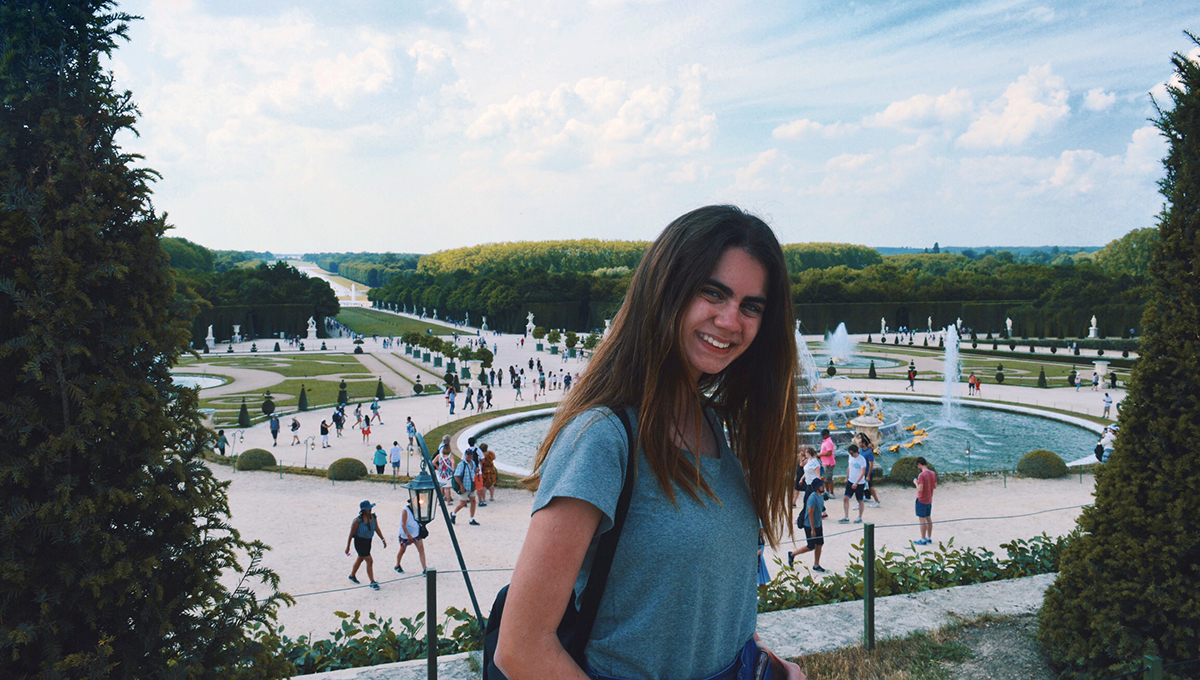 Flávia Figuerêdo A female student stands in the foreground of a large crowded area with a fountain.