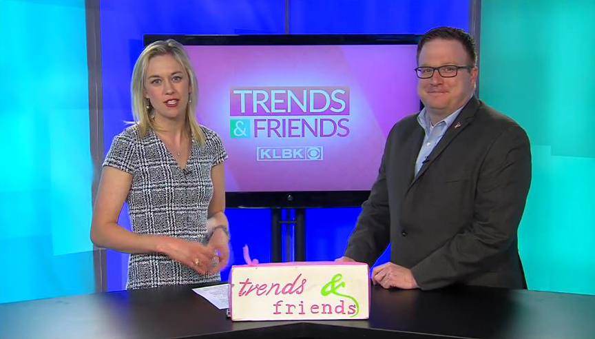 A man and woman stand side-by-side behind a table while facing the camera with a television screen behind them that reads "Trends & Friends KLBK"