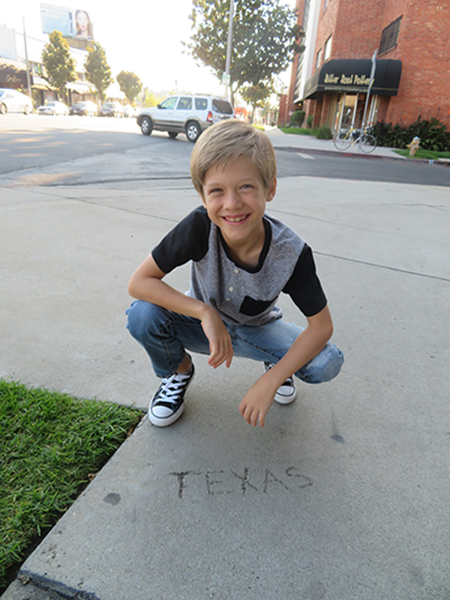 A young boy standing outside crouches just behind the word Texas that is engraved in concrete