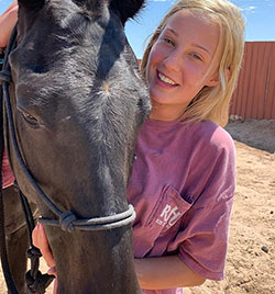 A girl stands closely next to a horse.