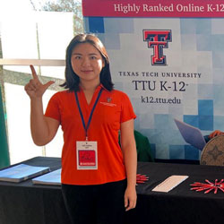 Victoria Qin gives the guns up sign in front of the TTU K-12 booth a conference.