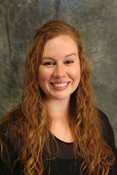 A headshot of a woman with brown hair wearing a black shirt and smiling at the camera.