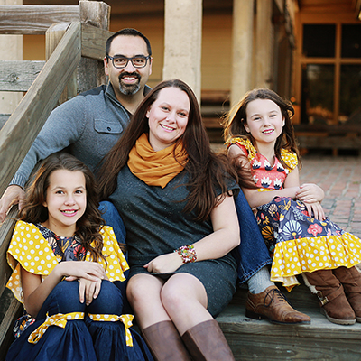 A man, woman, and two girls all sit outdoors on wooden steps while posing for a family photo.