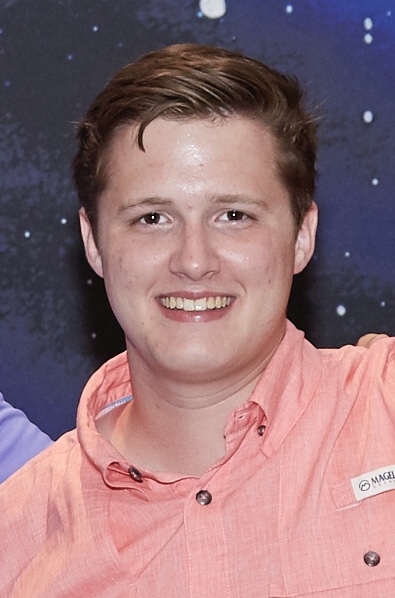A man wearing a pastel red shirt smiles at the camera