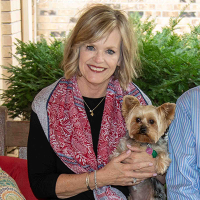 A woman sits on a bench outdoors while holding a small Yorkie.