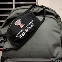 A light-green colored backpack rests while a Texas Tech University High School mask rests on top of the backpack.