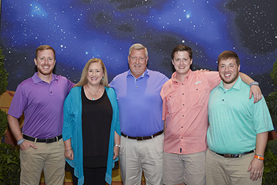 A family of five consisting of four men and one woman stand beside one another smiling.