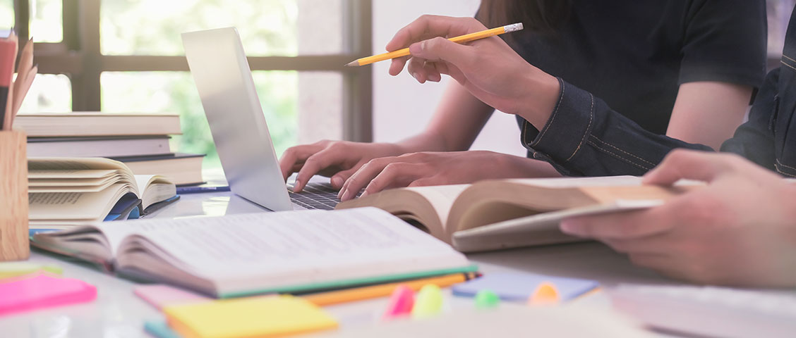 close up of students studying at home on a laptop with books and notes ona table