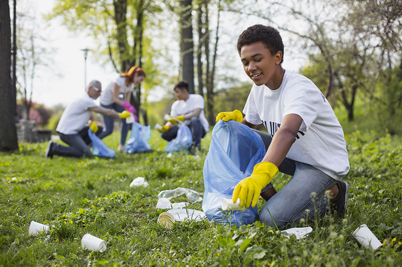 young man picking up litter outside with others doing same in the background