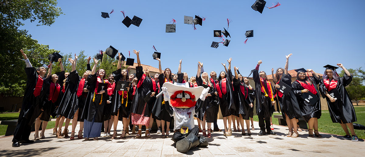 Graduates throwing mortar boards in the air with Raider Red at the 2022 TTU K-12 Commencement.