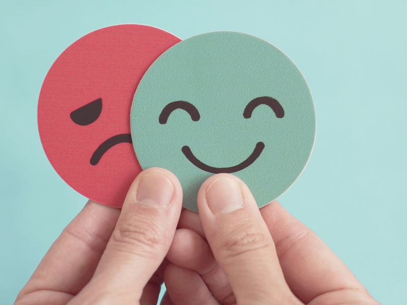 hands holding a smiling face and a crying face