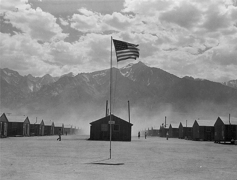 Photo by Dorthea Lange, 1942.  Photo of U.S. flag flying over the Manzanar Japanese-American Internment camp in the Owens Valley, California desert.