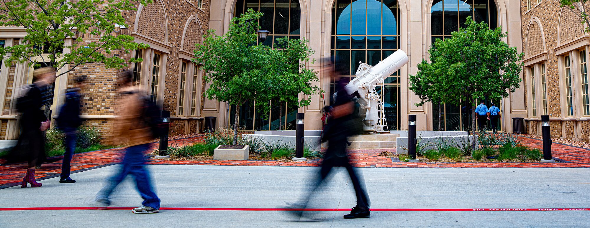 Students walking in front of the Rawl Business college's telescope